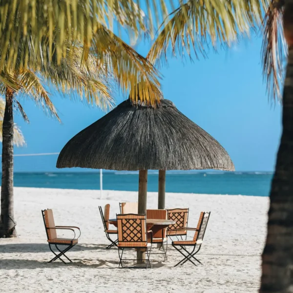 A table and chairs on the beach under an umbrella.